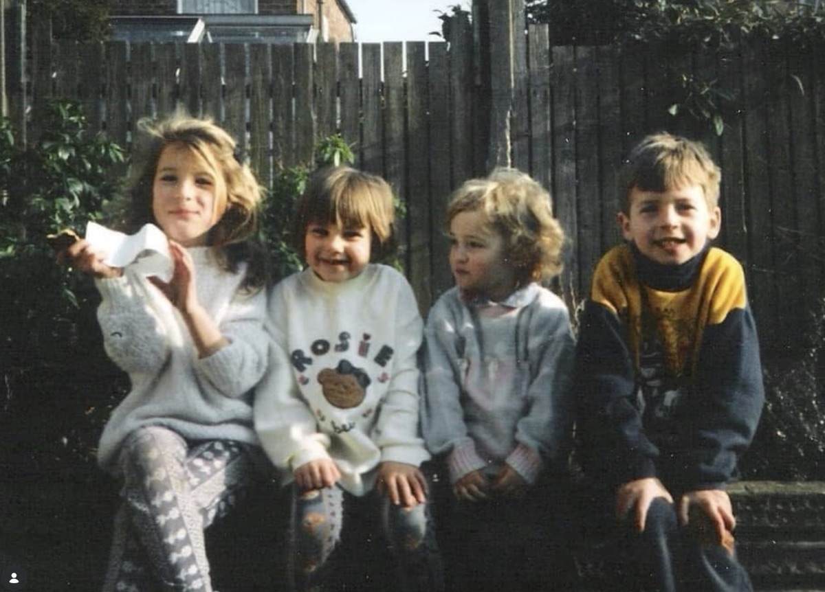 Family archive photo: four young children sitting together in front of a backyard fence