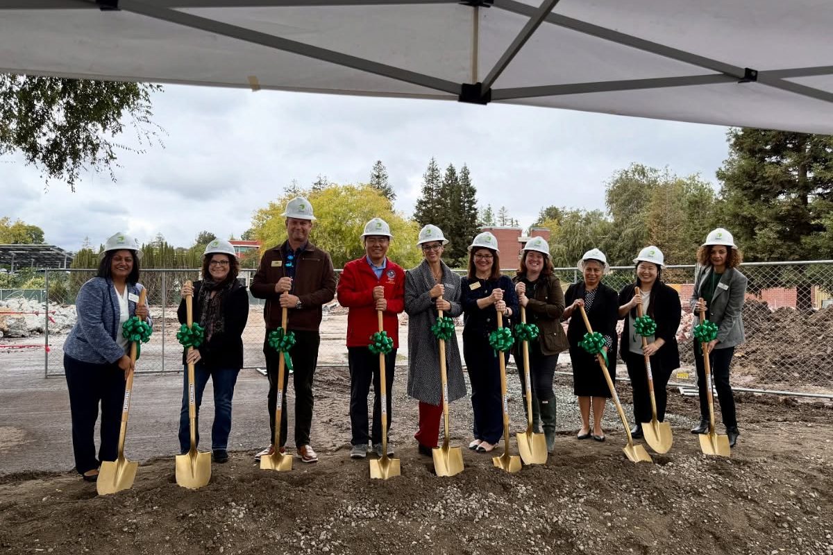 Officials in hard hats hold golden shovels at a campus construction groundbreaking