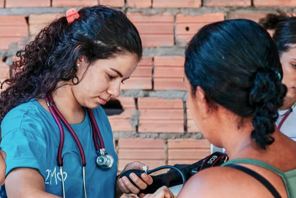 A nursing student with a stethoscope takes a woman’s blood pressure at a community health event