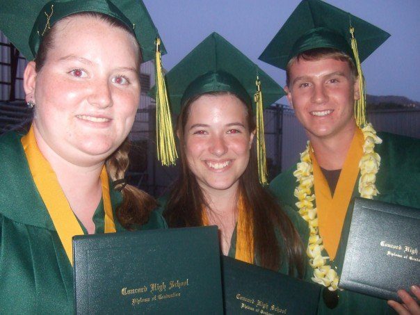 Three Concord High graduates in green caps and gowns hold their diplomas